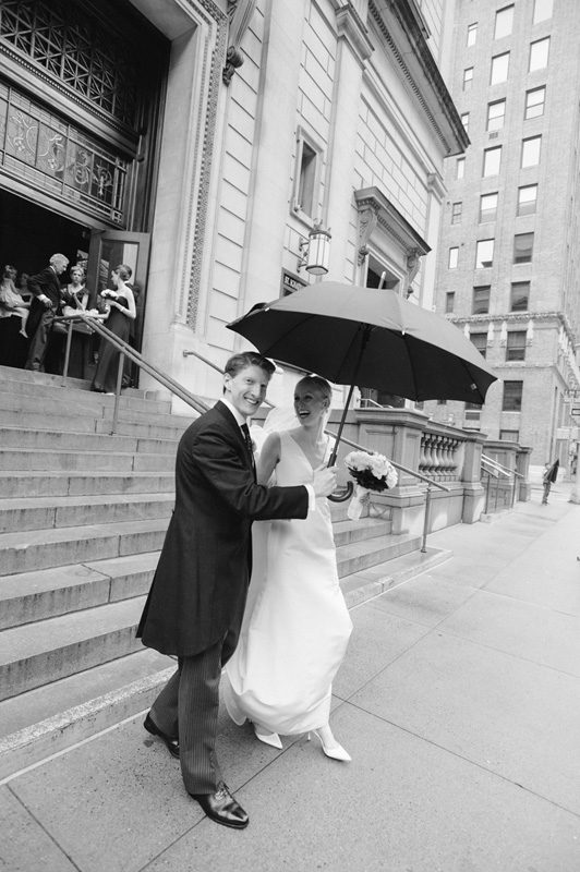 The groom holds an umbrella for his newly wedded wife