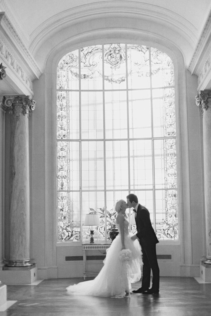 The bride and the groom kissing near an arched window