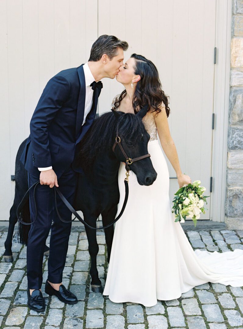 The bride and the groom kissing with the pony at the side