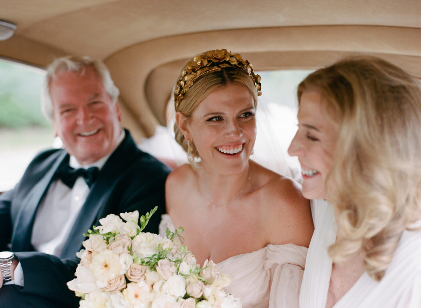 The bride seated between her parents inside the car