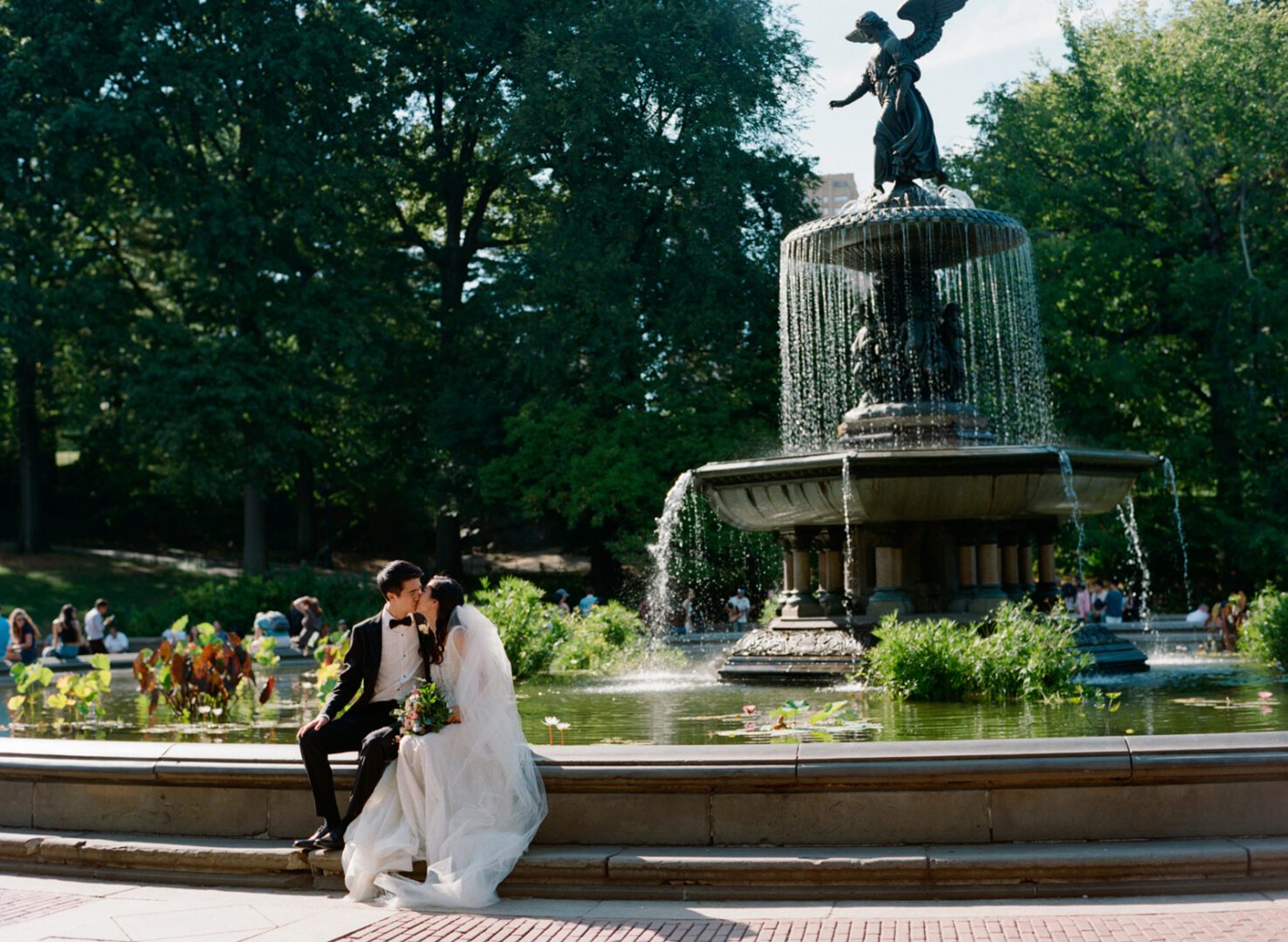 A newlywed couple standing in front of a fountain