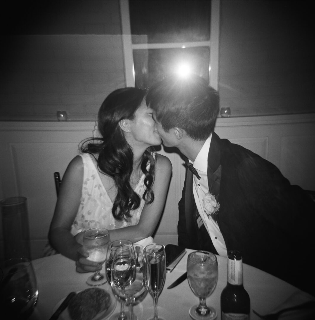 Newlywed couple kissing together at party table