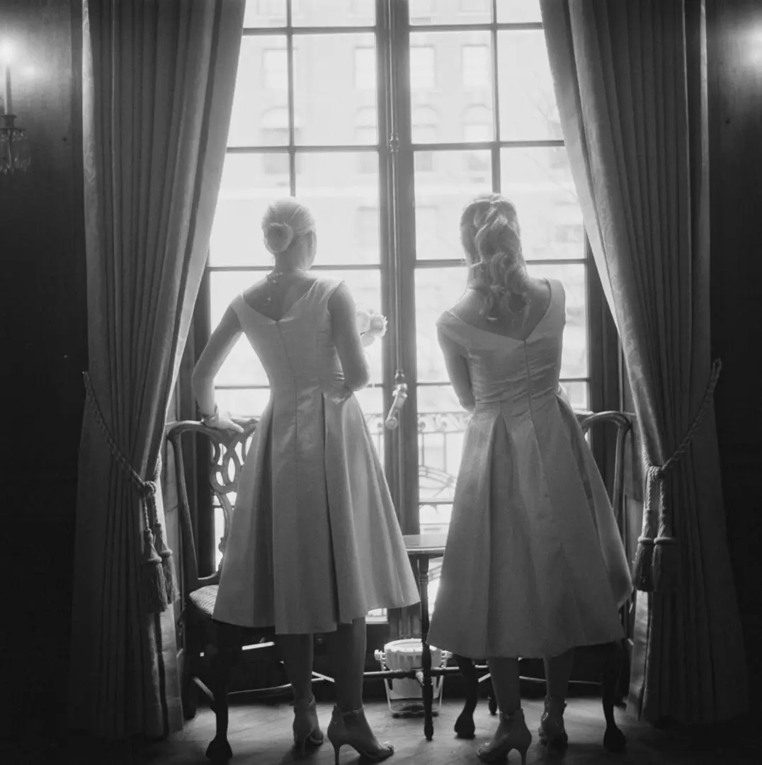 Black and white image of two girls watching from window