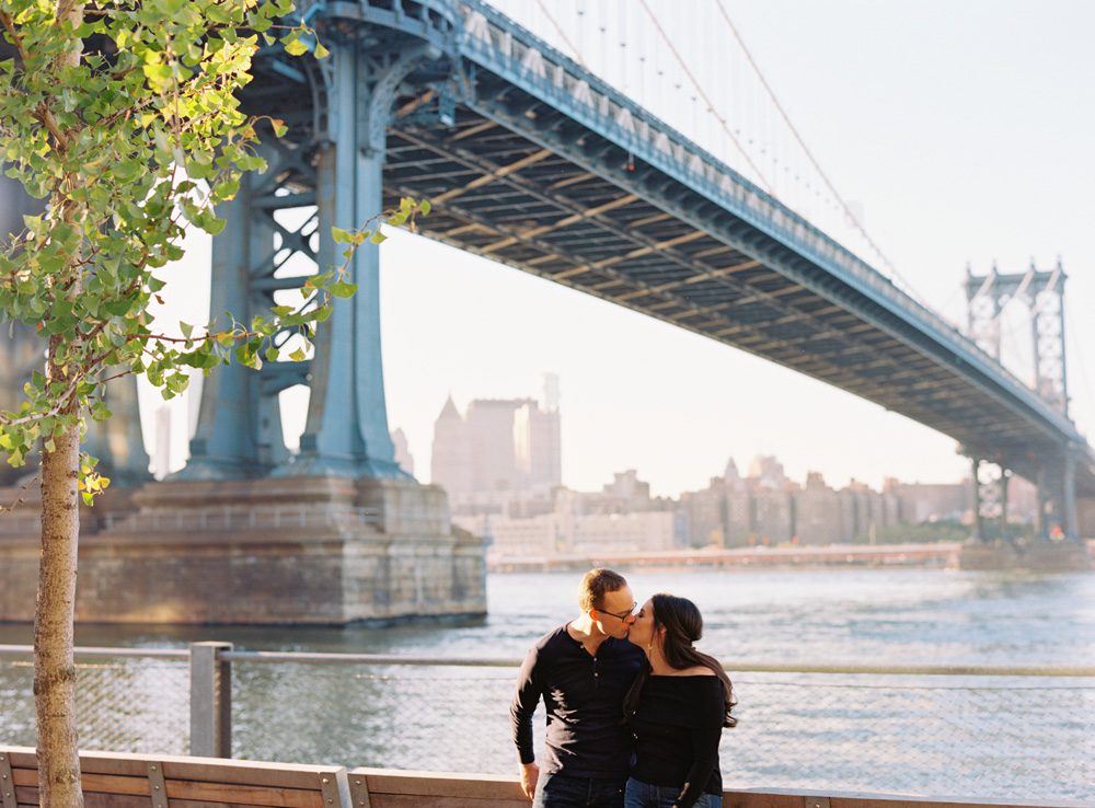 A couple kissing with a bridge in background