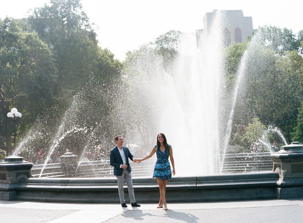 A couple holding hands with a fountain in background